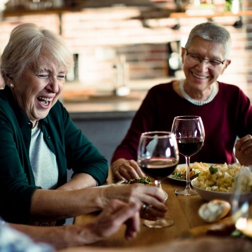 A group of senior adults sitting around a dining table, smiling and chatting as they enjoy lunch together.
