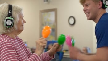 Photo Credit: The Day by Day Project Senior resident dancing with headphones on during a silent disco, accompanied by a staff member.