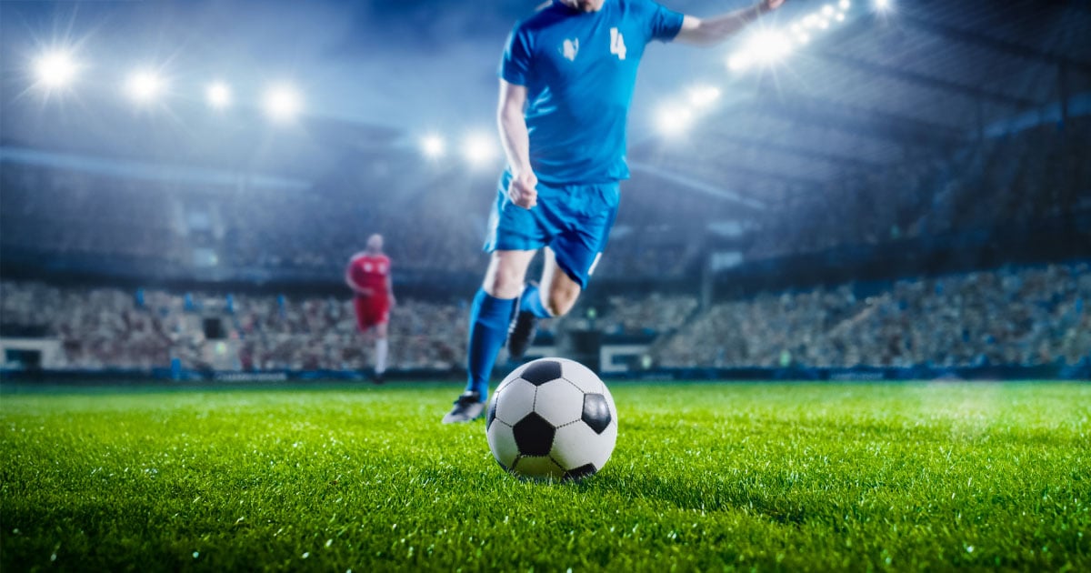 A soccer player runs to kick the ball on a grass field in a packed stadium.