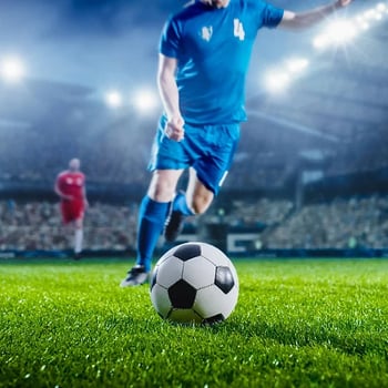 A soccer player runs to kick the ball on a grass field in a packed stadium. 