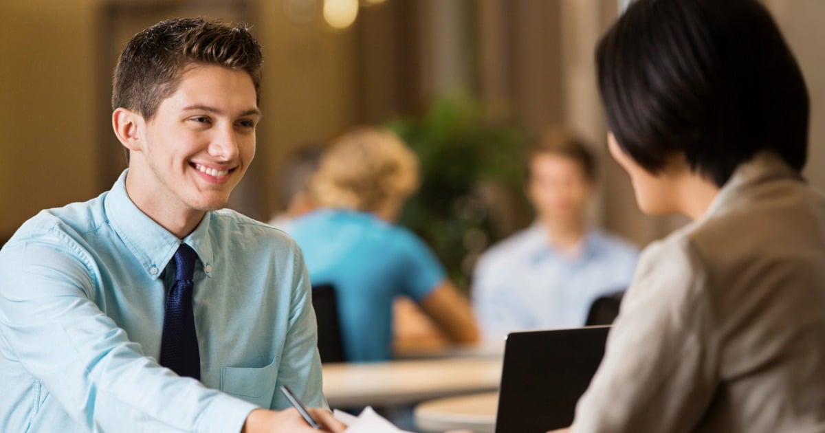 Two people sit across a table having a conversation in a professional setting.