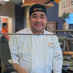 SUNY New Paltz Dining Services team member Julian Garcia smiles behind a serving counter.  