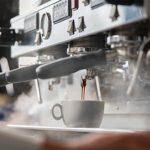 Espresso machine pouring coffee into a small cup with steam rising.