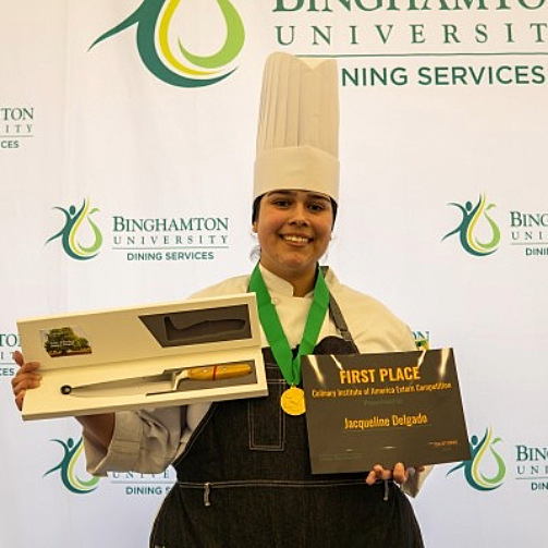 Chef Jacqueline Delgado, winner of the cooking competition, holding up a certificate and prize with a proud smile.