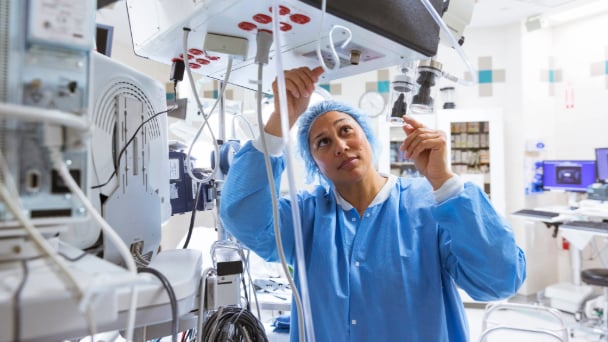 A woman in a hospital gown holds an oxygen machine, appearing focused and attentive to her breathing needs.