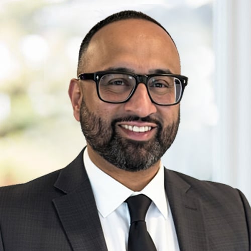 Head-and-shoulders portrait of a person wearing glasses, a dark suit, white shirt, and black tie.