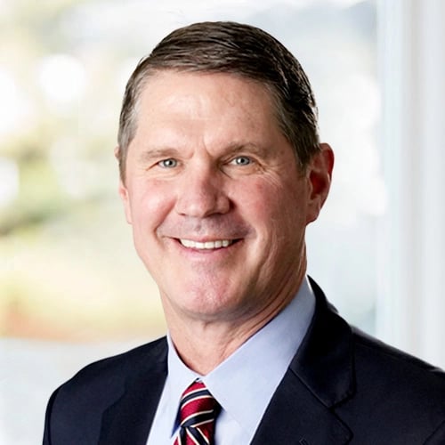 Person in a suit and tie smiling with a blurred office or indoor background.