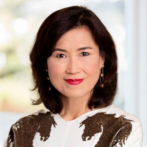 Person with shoulder-length dark hair in patterned white top and gold earrings.
