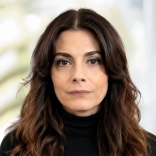 Sandrine Church, Head of Strategy, NORAM headshot with wavy brown hair in black turtleneck, facing forward, blurred light background