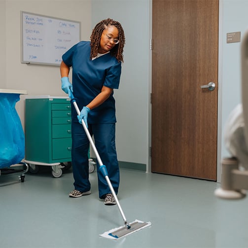 Healthcare environmental services worker mopping the floor in a clinical room, highlighting sanitation practices, infection prevention, facility cleanliness, and support for safe patient care environments.