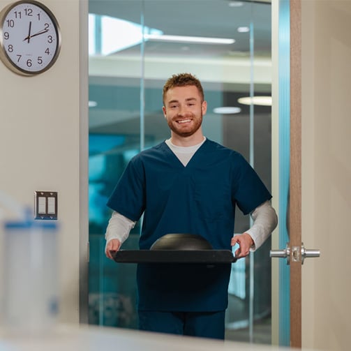 Healthcare food service worker carrying a covered meal tray through a clinical facility doorway, highlighting patient nutrition services, meal delivery, hospitality support, and coordinated healthcare operations.