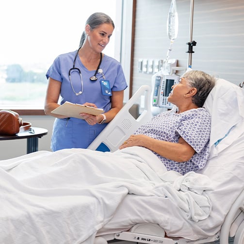 Healthcare professional reviewing information with a patient at a hospital bedside, highlighting patient-centered care, clinical communication, care coordination, and personalized support in a healthcare setting.