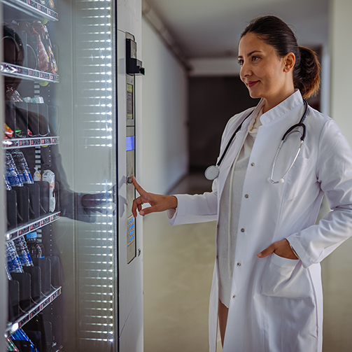 A doctor standing at a vending machine selecting a snack.