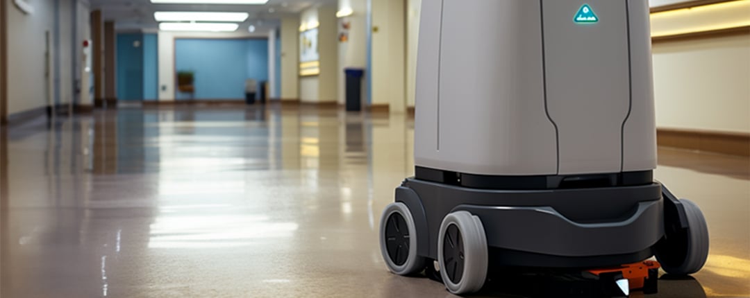 Autonomous floor-cleaning robot operating in a bright hospital corridor with polished reflective floors.