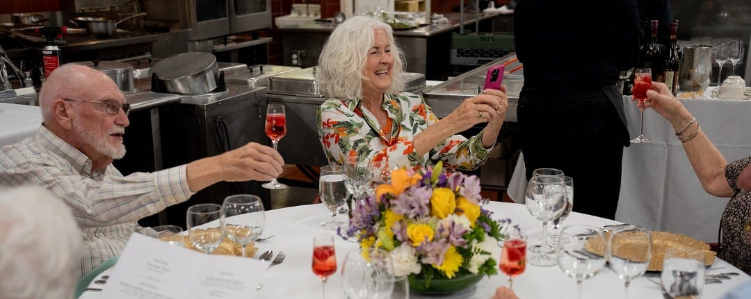Senior residents celebrating at a community dining event, raising glasses around a table with flowers. 