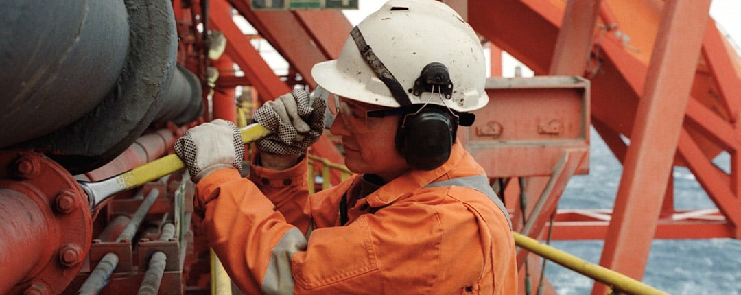 Facilities management promotional graphic featuring industrial workers in safety gear performing equipment maintenance inside a manufacturing facility, highlighting operational efficiency and cost reduction initiatives.