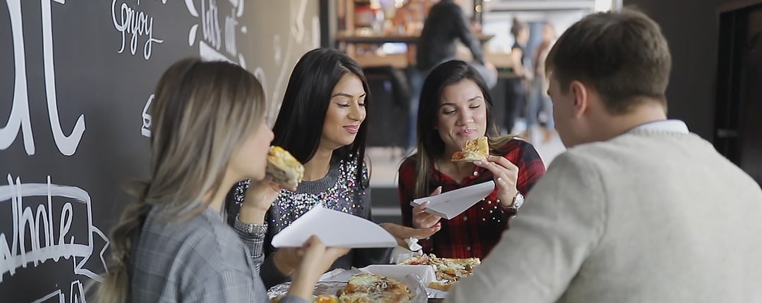 Four people sit around a table enjoying slices of pizza in a casual restaurant setting. 