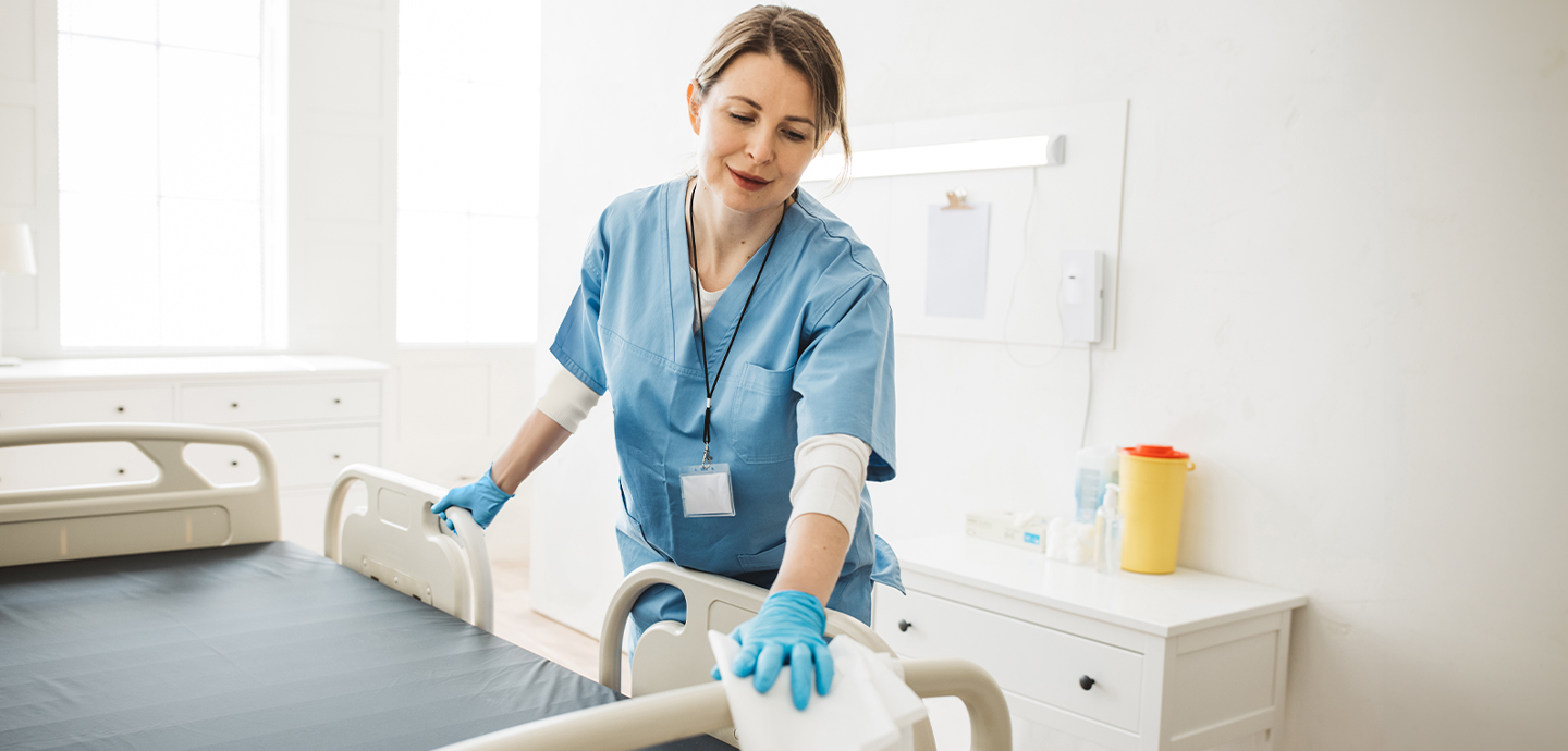 Female staff wiping down a patient bedrail.