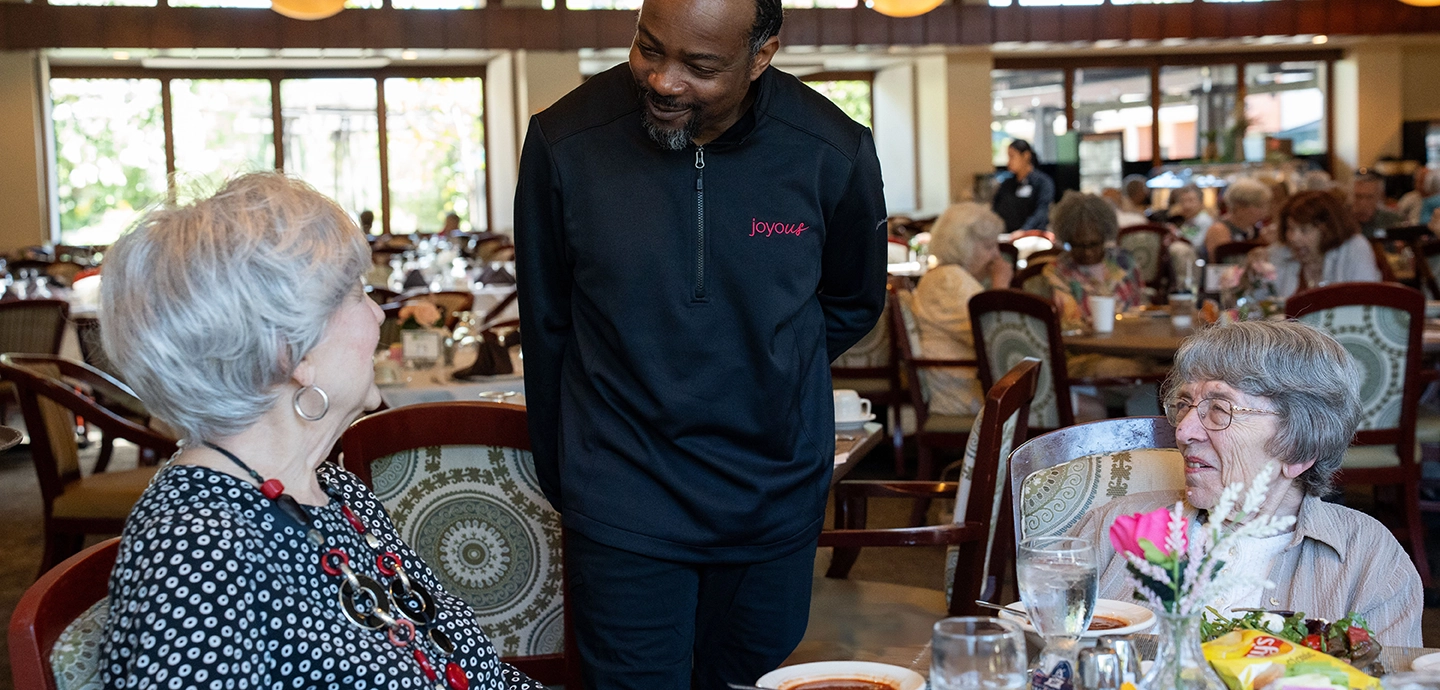 Joyous employee greeting 2 senior women at a dining table