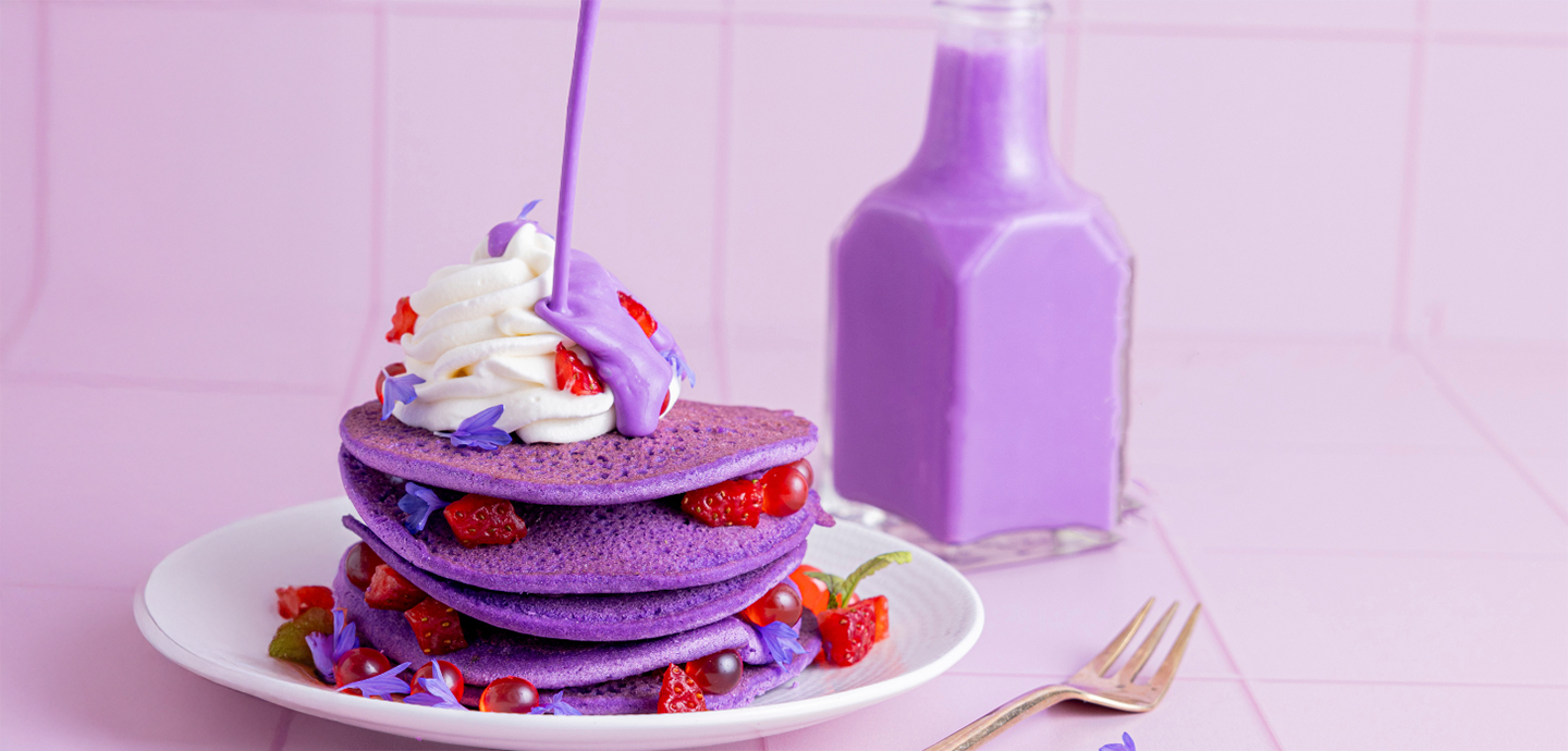 Vibrant ube pancakes with fresh berries and a swirl of whipped cream.