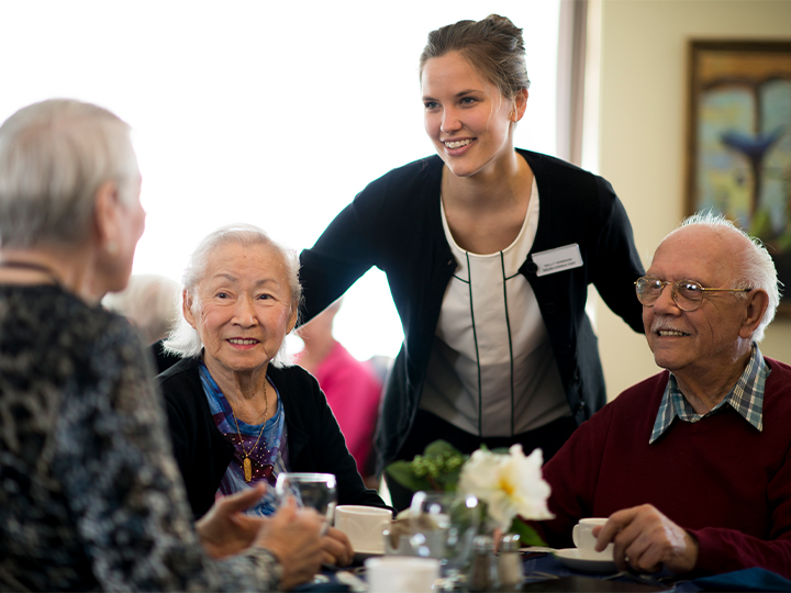 Group of senior residents sitting at a dining table with a friendly server