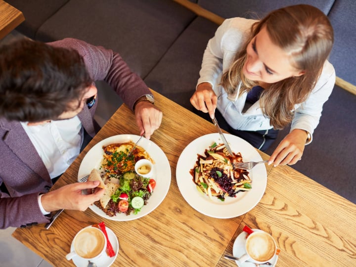 Two students at a dining hall with plates full of food and cups of coffee.