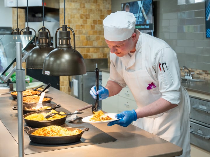 Chef plating a dish at a food counter. 