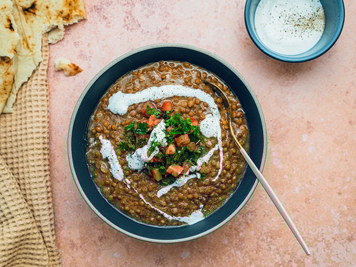 Close up of lentil soup garnished with fresh herbs diced tomatoes and yogurt served with flatbread