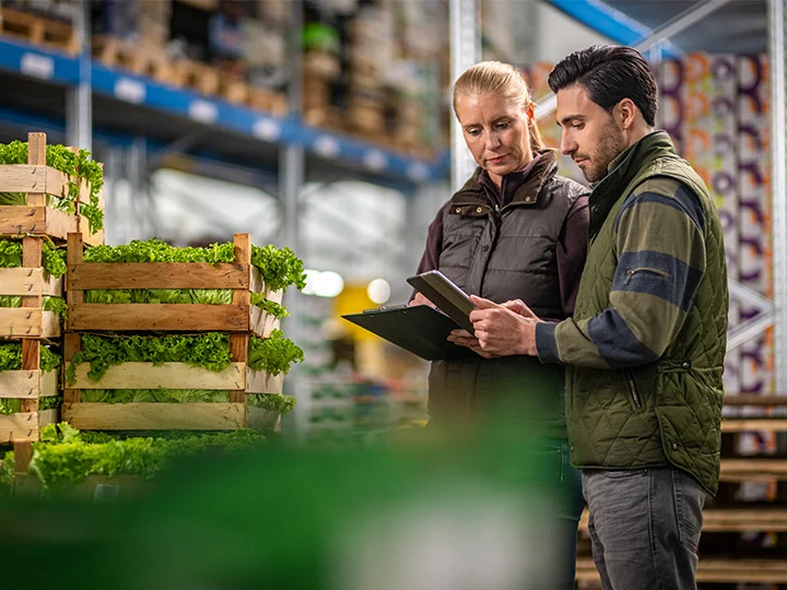 Two individuals examining a tablet together inside a warehouse setting.