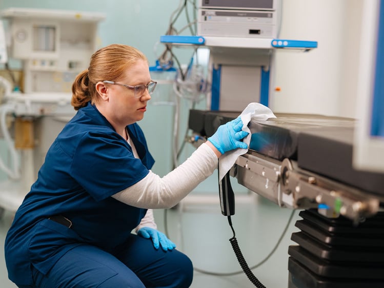 Healthcare environmental services professional disinfecting medical equipment in a clinical treatment room, highlighting infection prevention, hospital sanitation, patient safety, and healthcare facility cleanliness.