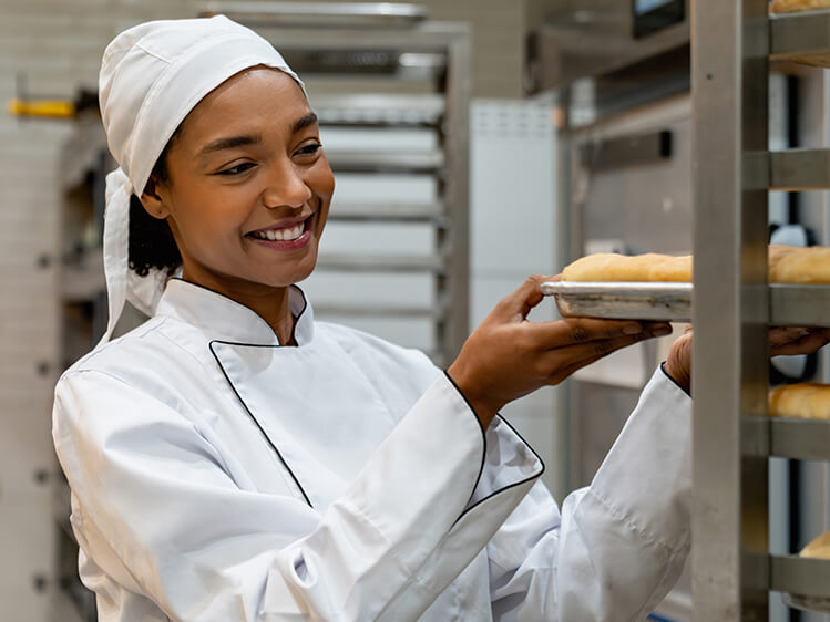 Chef placing freshly baked bread rolls onto a bakery rack in a commercial kitchen, highlighting food preparation, culinary expertise, quality baking, and hospitality-focused dining services.