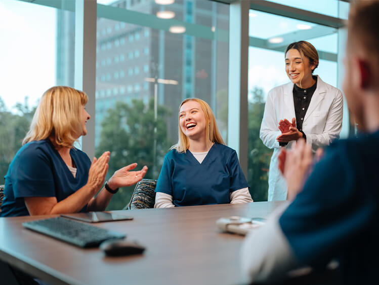 Healthcare professionals gathered around a conference table during a team meeting, highlighting staff recognition, collaboration, workforce engagement, and a positive healthcare workplace culture.