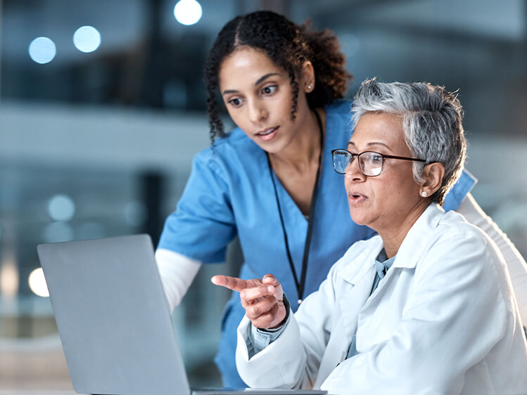 Healthcare professionals reviewing information together on a laptop in a clinical setting.
