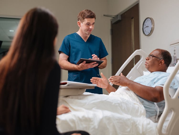 Hospital patient lying in a bed having a discussion with a nurse standing next to him