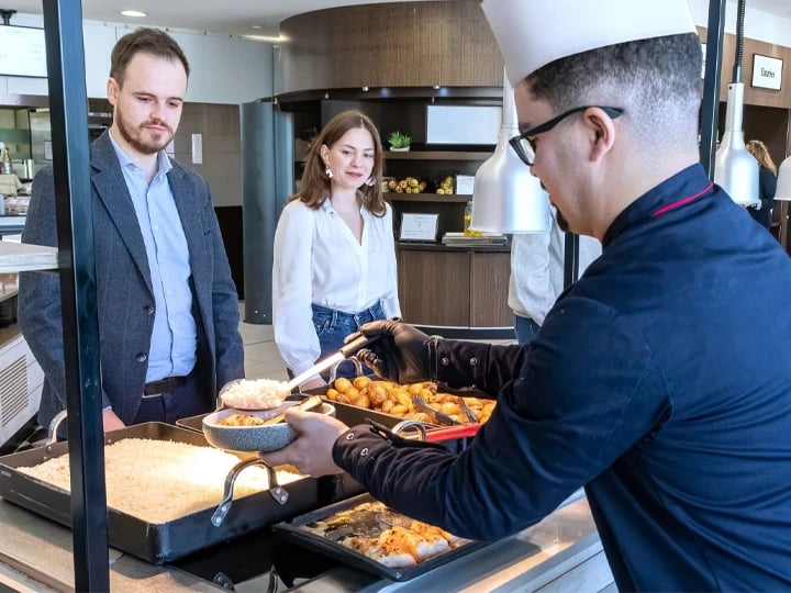 A man serves food to a woman and another man at a dining table, creating a warm and inviting atmosphere.