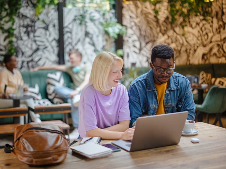 College students working on laptops while enjoying coffee in a vibrant café setting.