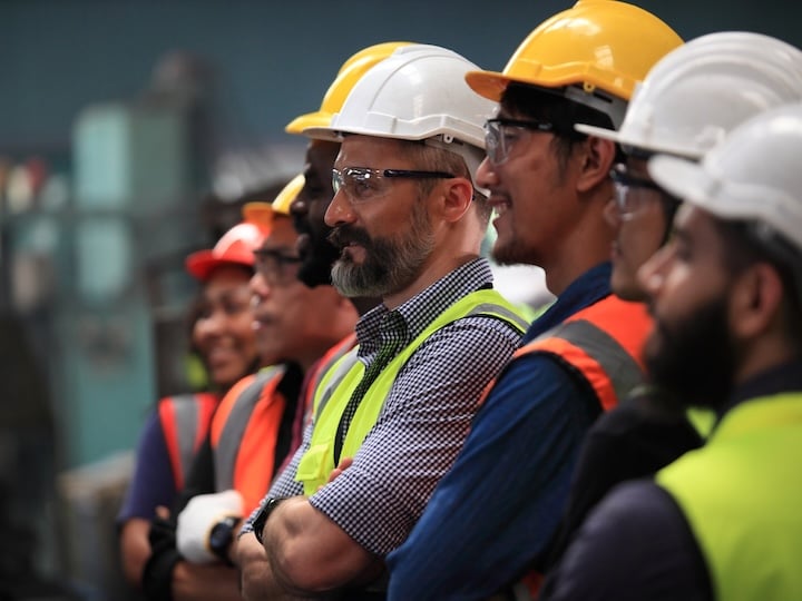 Workers in safety helmets and high-visibility vests standing together in an industrial facility.