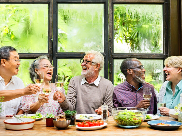 Diverse group of older adults gathered around a dining table enjoying a shared meal and raising glasses, highlighting social connection, healthy eating, community engagement, and wellness-focused dining experiences.