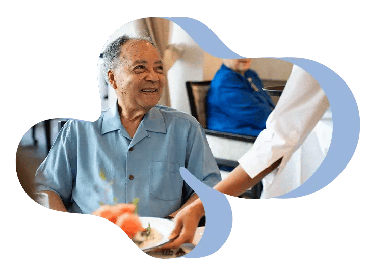 Smiling person in blue shirt receives a plate of food from another person dressed in white.