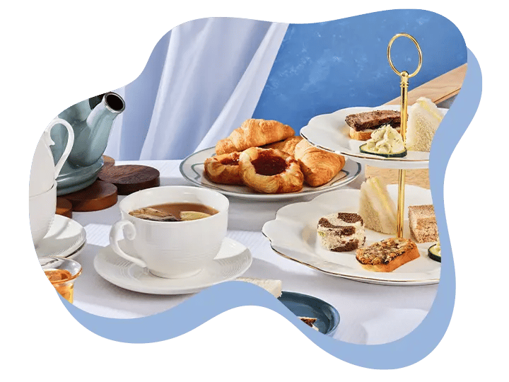 Afternoon tea with teapot, cup, croissants, pastries, and a two-tier tray of assorted sandwiches.