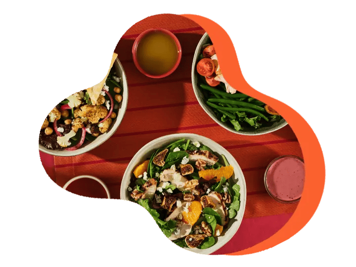 Three colorful salad bowls with various ingredients on a red tablecloth, served with two drinks.