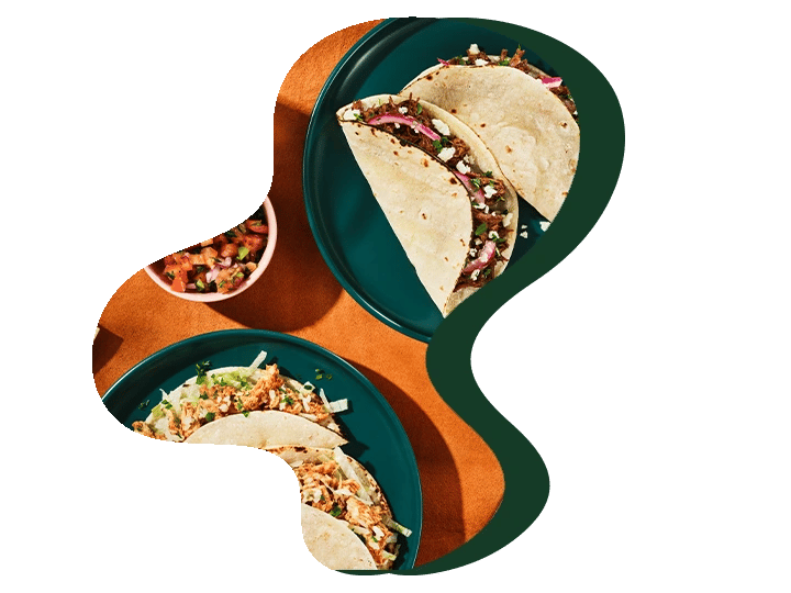 Two plates of tacos with assorted fillings and a small bowl of salsa on a table.