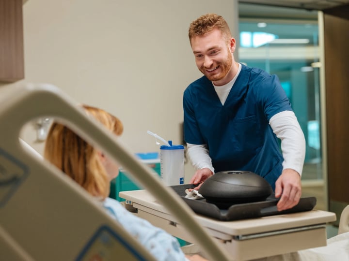A healthcare worker handing a meal tray to a patient lying in a hospital bed.