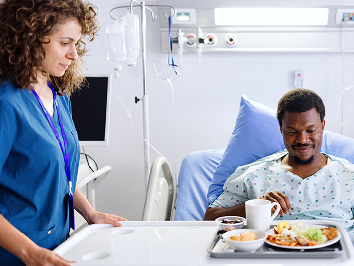 Healthcare worker serving a healthy meal to a patient in bed.