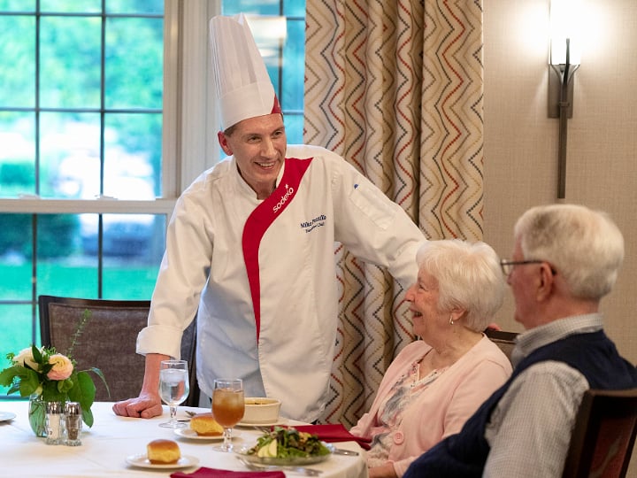 Sodexo chef greeting a senior couple in a dining room.