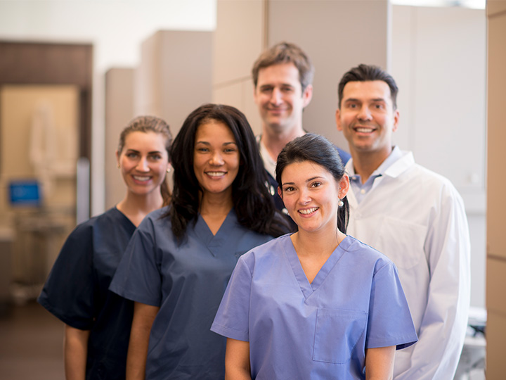 A group of smiling individuals wearing scrub suits, standing together in a friendly and professional manner.