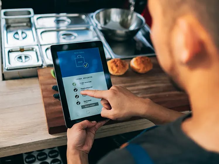 Person using a tablet to monitor food order progress in a commercial kitchen workstation.
