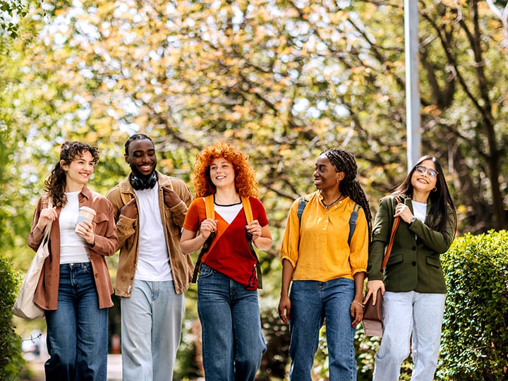 A diverse group of college students smiling and conversing while walking through campus.