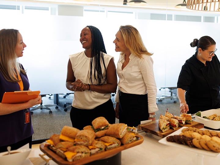3 women talking and smiling while enjoying catered food
