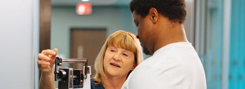 Man standing on a scale while a hospital worker takes note of his weight 